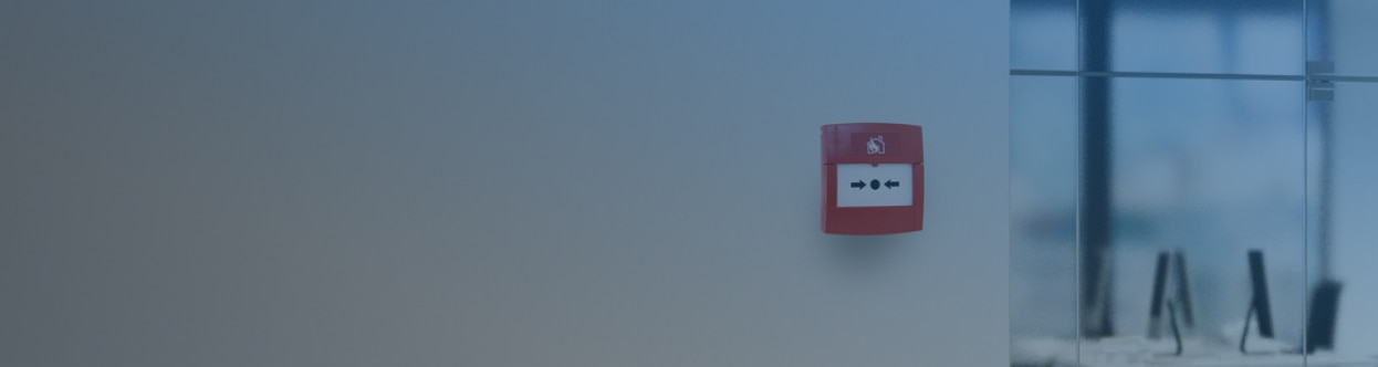 A fire alarm call point attached to a wall in an office, overlaid with a blue gradient